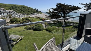 Een balkon met uitzicht op een strand, huizen en een boom.