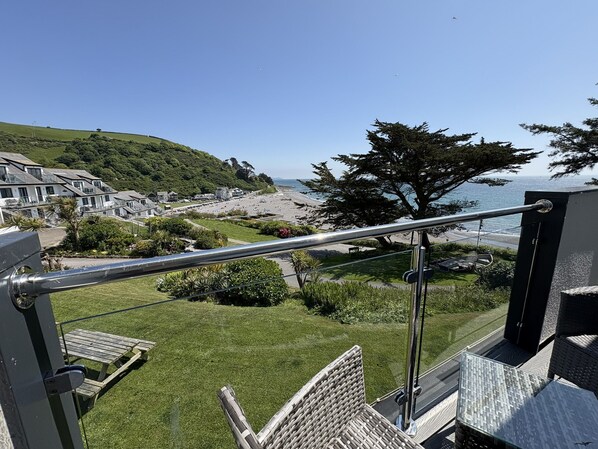 A balcony with a view of a beach, houses, and a tree.