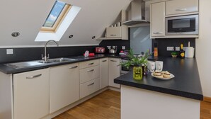 A modern kitchen with a skylight, white cabinets, a black countertop, and a built-in microwave. - Cornish Duplex 2 Bedroom Apartment with Stunning Sea Views (Torpoint)