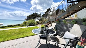 A patio with a round table, chairs, and potted plants. A staircase leads to an upper level.