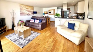 A living room with a sofa, a coffee table, a TV, and a kitchen area with cabinets and appliances.