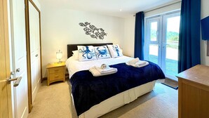 A bedroom with a bed, a nightstand, a wall decoration, a view through a door, and a bathroom area.
