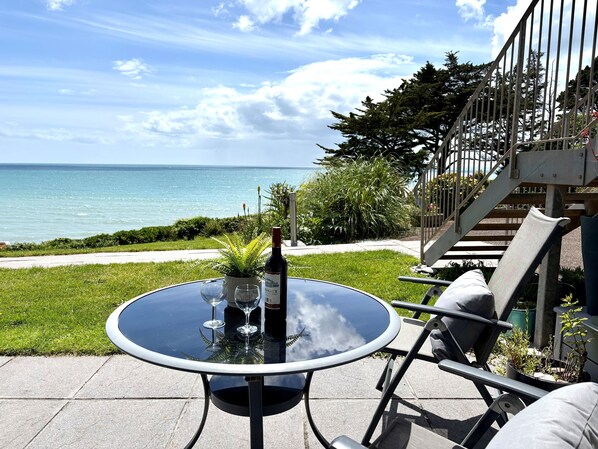 A round table with a bottle and glasses, outdoor seating, a staircase, and a view of the sea.