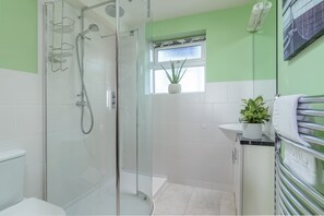A modern bathroom with a glass-enclosed shower, a small window with a plant, and a towel rack.