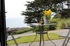 An outdoor table with a bottle of wine, a glass, and a vase of yellow flowers.
