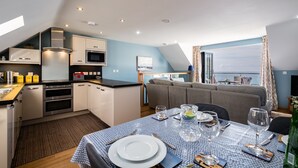 A modern kitchen with built-in appliances, a dining area with a table set for two, and a view of the sea through large windows. - Fantastic Sea Views from this Newly Refurbished Duplex Apartment (Torpoint)