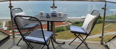 A balcony with a table and two chairs, overlooking the sea.