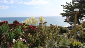 A garden with a variety of plants and flowers, a wooden structure, and a view of the sea. - Seaside Duplex Apartment with Amazing Sea Views (Torpoint)
