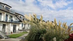 A modern two-story building with a balcony, a staircase, and a well-maintained lawn. - Seaside Duplex Apartment with Amazing Sea Views (Torpoint)
