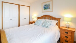A bedroom with a bed, two nightstands, a wooden headboard, a white door, and a framed picture on the wall. - Seaside Duplex Apartment with Amazing Sea Views (Torpoint)