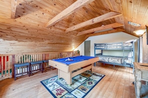 Relax in this cabin-style room with a pool table, comfortable sofa, and rustic wooden beams.