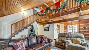 Ein gemütliches Wohnzimmer mit Ledersofa, Couchtisch aus Holz und Kamin. Im Hintergrund ist eine Treppe mit Geländer und Girlande zu sehen.