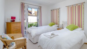 A bedroom with two beds, a wooden dresser, a wicker chair, and a window with striped curtains.