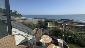 A balcony with wicker chairs and a table, overlooking a beach and the ocean.