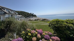 A coastal hotel with a view of the sea, a grassy lawn, and a flower bed.