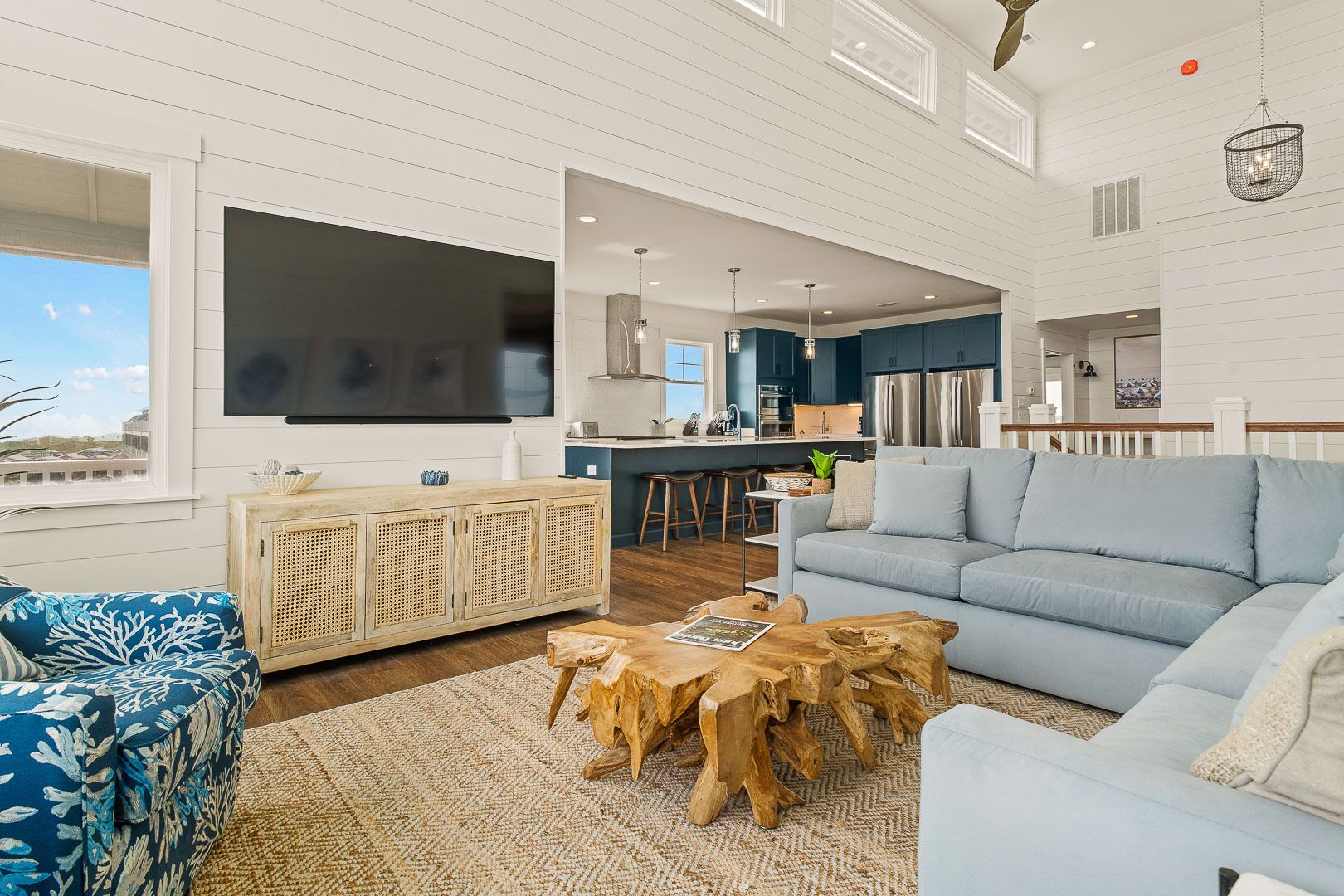 A spacious living room with a large sofa, a coffee table, and a TV. There is a kitchen area with a bar and stools.