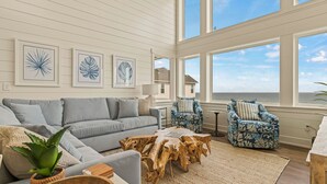 A coastal living room with a grey sofa, two patterned armchairs, a wooden coffee table, and framed artwork on the wall.