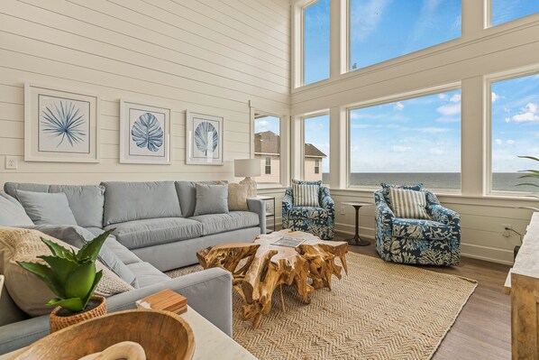 Relax in this stylish living room with a sofa, coffee table, and armchairs, surrounded by artwork and a large window with ocean views.