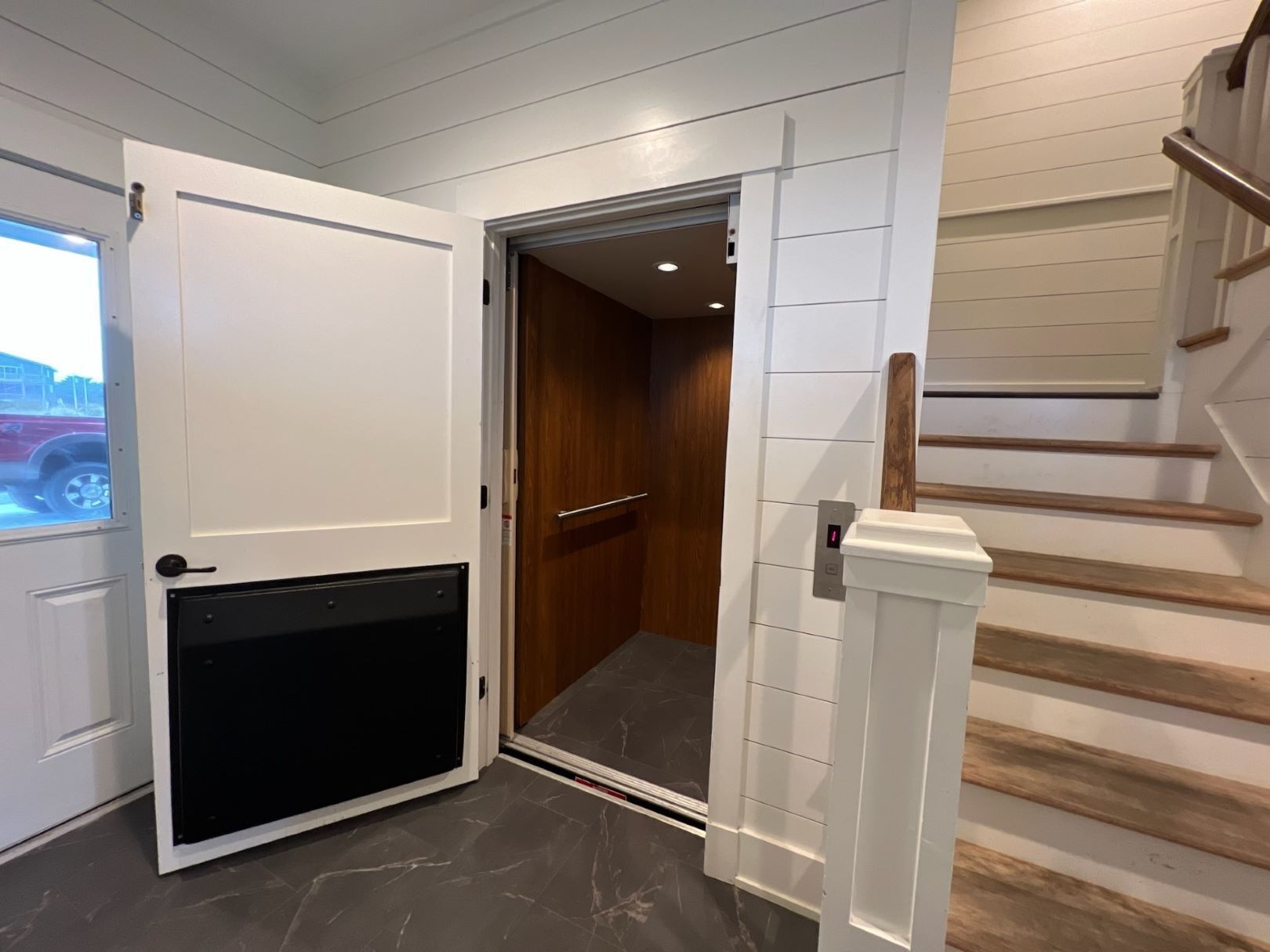 Een modern interieur met een schuifdeur die leidt naar een houten deur, een trap met houten treden en een marmeren vloer.