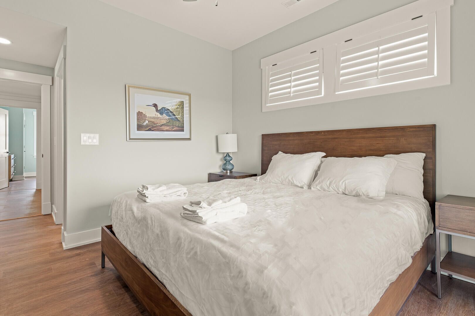 A neatly made bed with white linens, a wooden headboard, and a bedside table with a lamp.