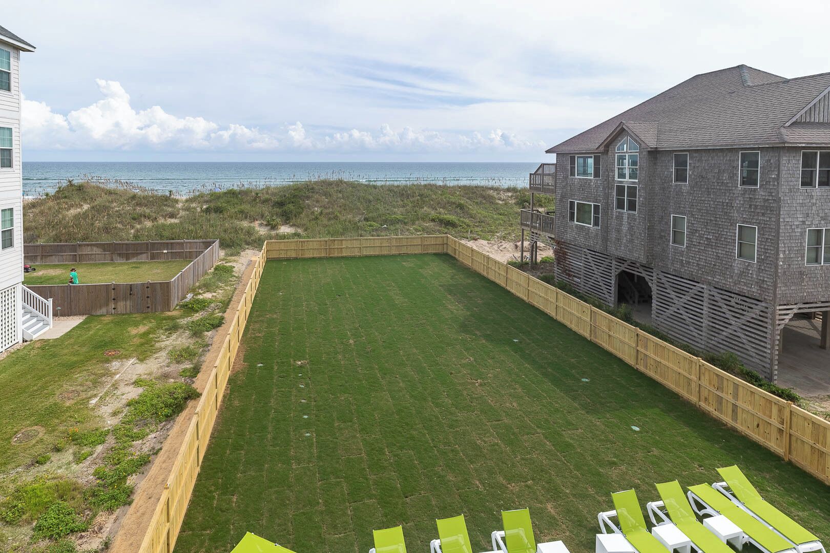 A backyard with a lawn, a wooden deck, and a view of the beach.