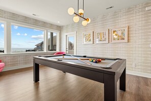 Enjoy a game of pool in this stylish room with a pool table, large windows, and artwork on the walls.
