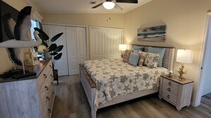 A bedroom with a bed, bedside tables, a ceiling fan, and a painting on the wall.