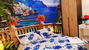 A bedroom with a bed, a wooden wardrobe, a nightstand, and a view of a coastal town. - Altea Royale (Naples)