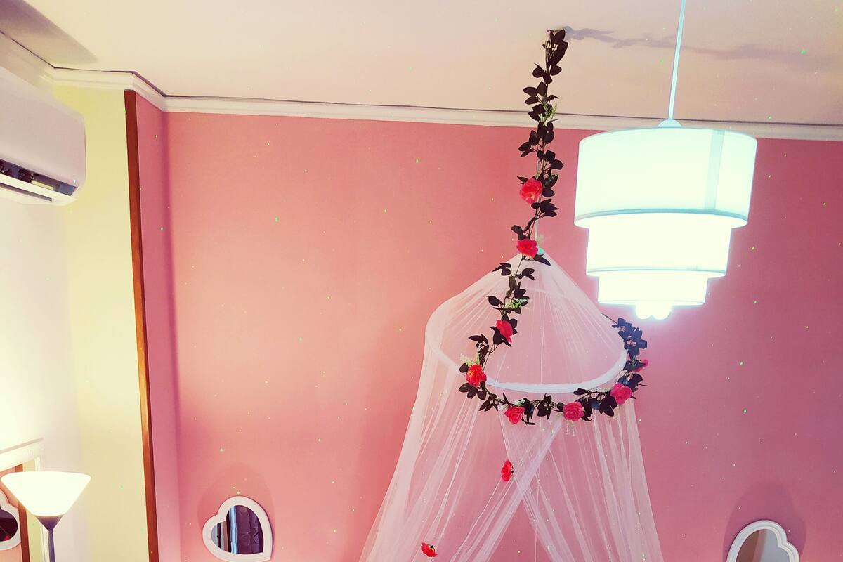 A bedroom with a bed, two bedside tables, a nightstand, a lamp, a mirror, and a decorative canopy.