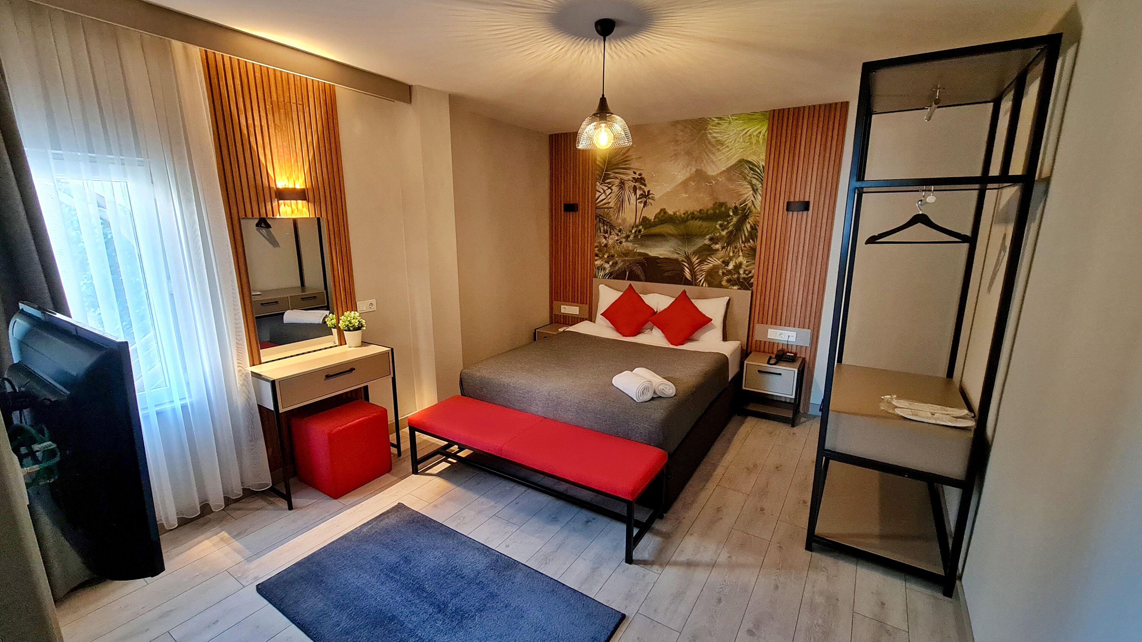 A hotel room with a bed, bedside table, mirror, wardrobe, and a desk with a chair.