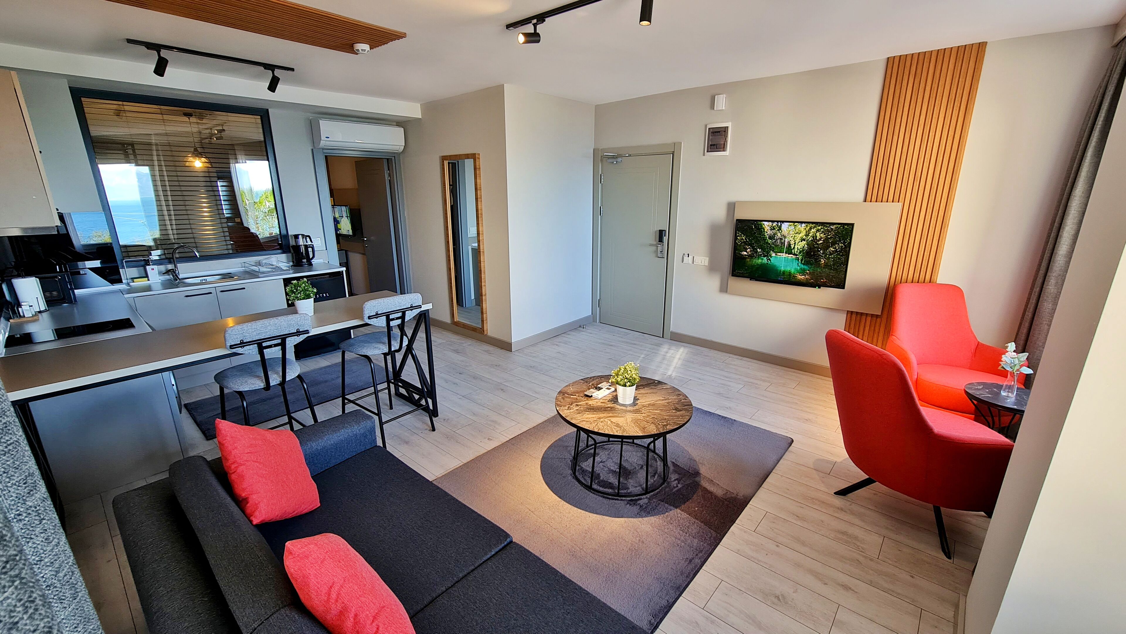 Een moderne woonkamer met een bank, een rode fauteuil, een salontafel en een aan de muur bevestigde televisie.