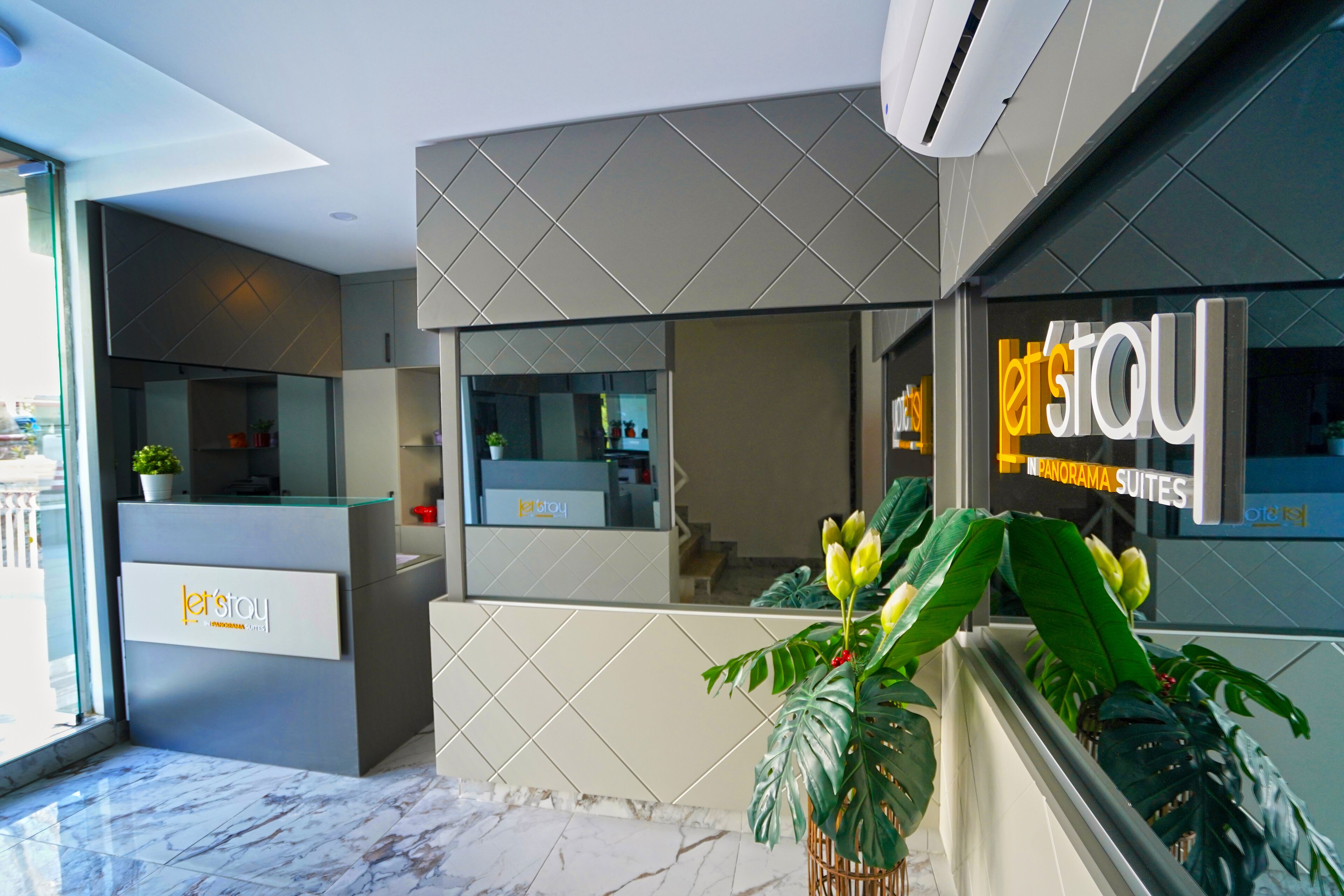 A modern hotel reception with a glass counter, a reception desk, and a large potted plant.