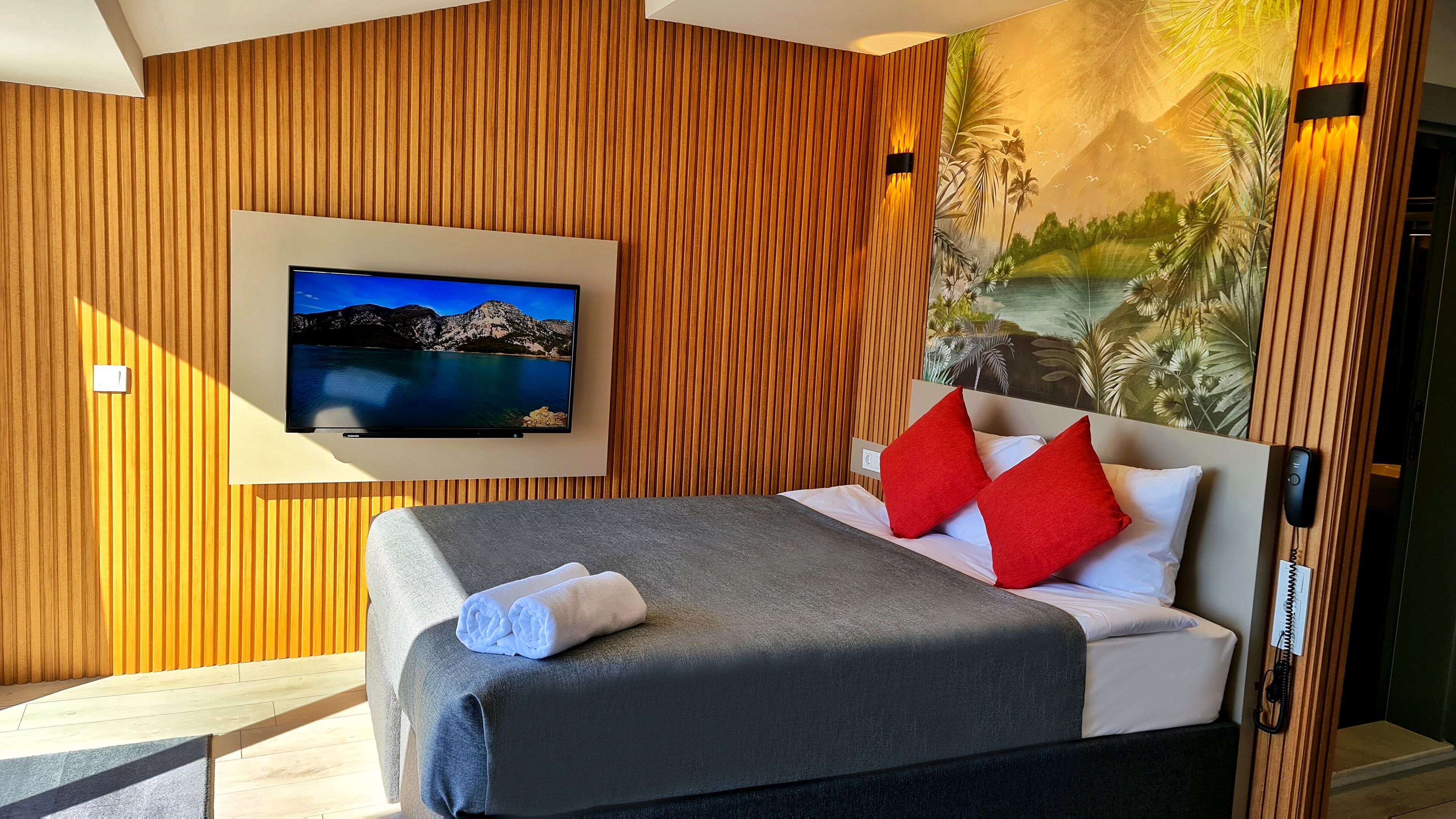 Een hotelkamer met een bed, een televisie en een muurschildering van een tropisch landschap.