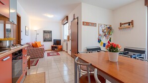 A modern kitchen with a dining area, a sofa, and a TV.