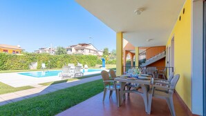 A patio with a dining table and chairs, a pool, and a staircase leading to an upper level.