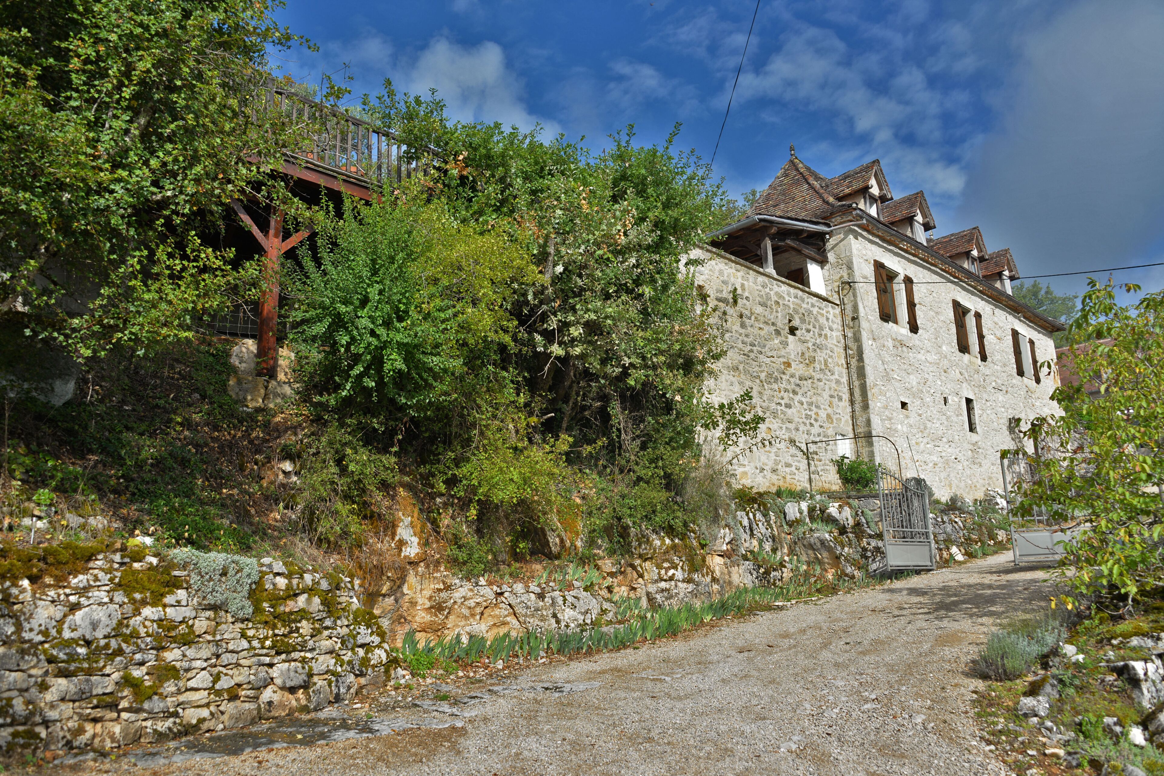 Ein Gebäude aus Stein mit traditionellem Dach, umgeben von Grün und einem Kiesweg.