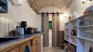 Une cuisine avec un plafond en pierre rustique, des armoires en bois, un sol carrelé et un îlot central doté d’une machine à café et d’un porte-serviettes suspendu.