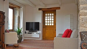Un salon avec une télévision, un canapé avec des coussins rouges, une porte en bois et un mur en pierre.