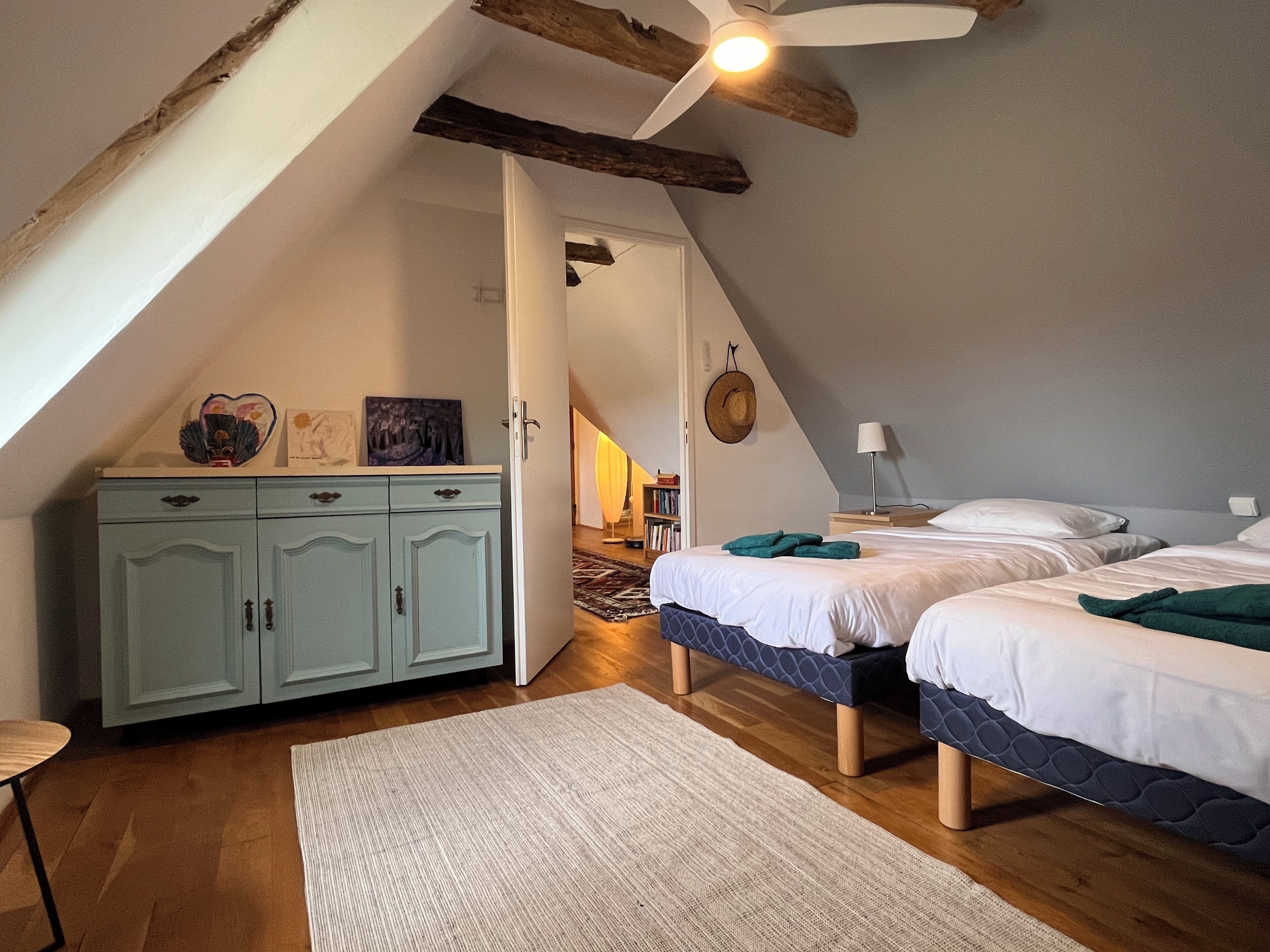 Une chambre avec deux lits, un plafond en bois, une armoire et un couloir menant à une autre pièce.