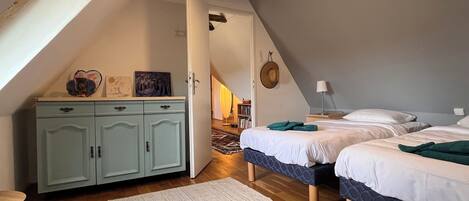 Une chambre avec deux lits, un plafond en bois, une armoire et un couloir menant à une autre pièce.