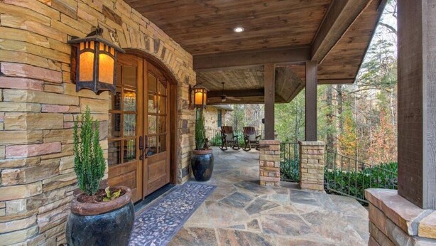 A stone exterior with a wooden porch, stone steps, and a view of trees. - Luxury estate, swim spa, game room, theater, fireplaces, views. (Gatlinburg)