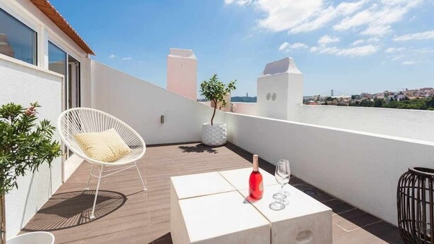 Une terrasse sur le toit, avec une chaise blanche, une petite table sur laquelle se trouvent une bouteille et des verres, et une vue sur le paysage urbain.