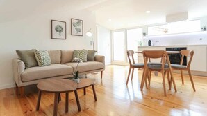 Un salon moderne avec un canapé, deux fauteuils, une table basse et une cuisine en arrière-plan.