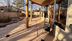 A covered patio area with a concrete floor, wooden columns, and a metal chair. - Sage Swan, 30+ Day Rentals, Near I-40 (Albuquerque)