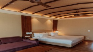 Ein modernes Hotelzimmer mit Holzboden, einem Bett mit weißen Leinen, einem violetten Sofa und einer hölzernen Bank.