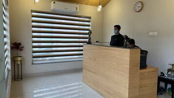 Un mostrador de recepción con detalles de madera, un reloj en la pared y una ventana con persianas horizontales.