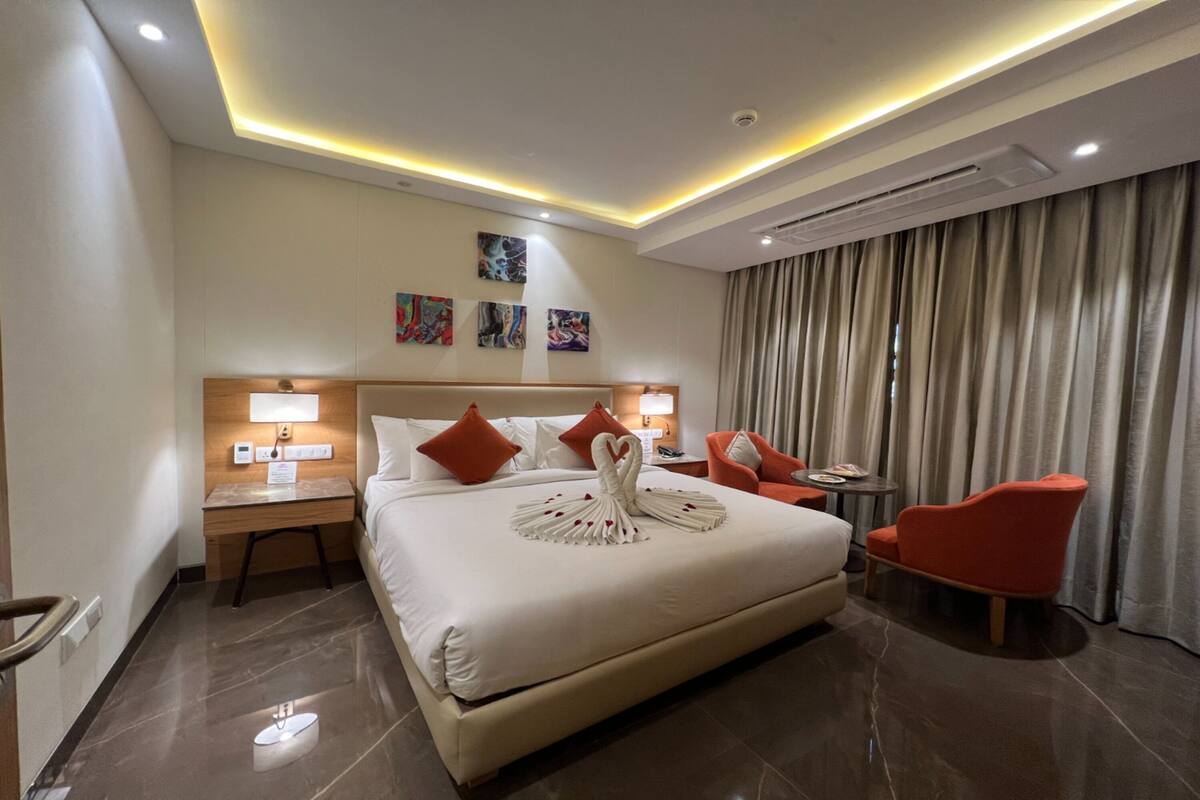 A hotel room with a large bed, two nightstands, a desk, a chair, and a view of the outside through curtains.