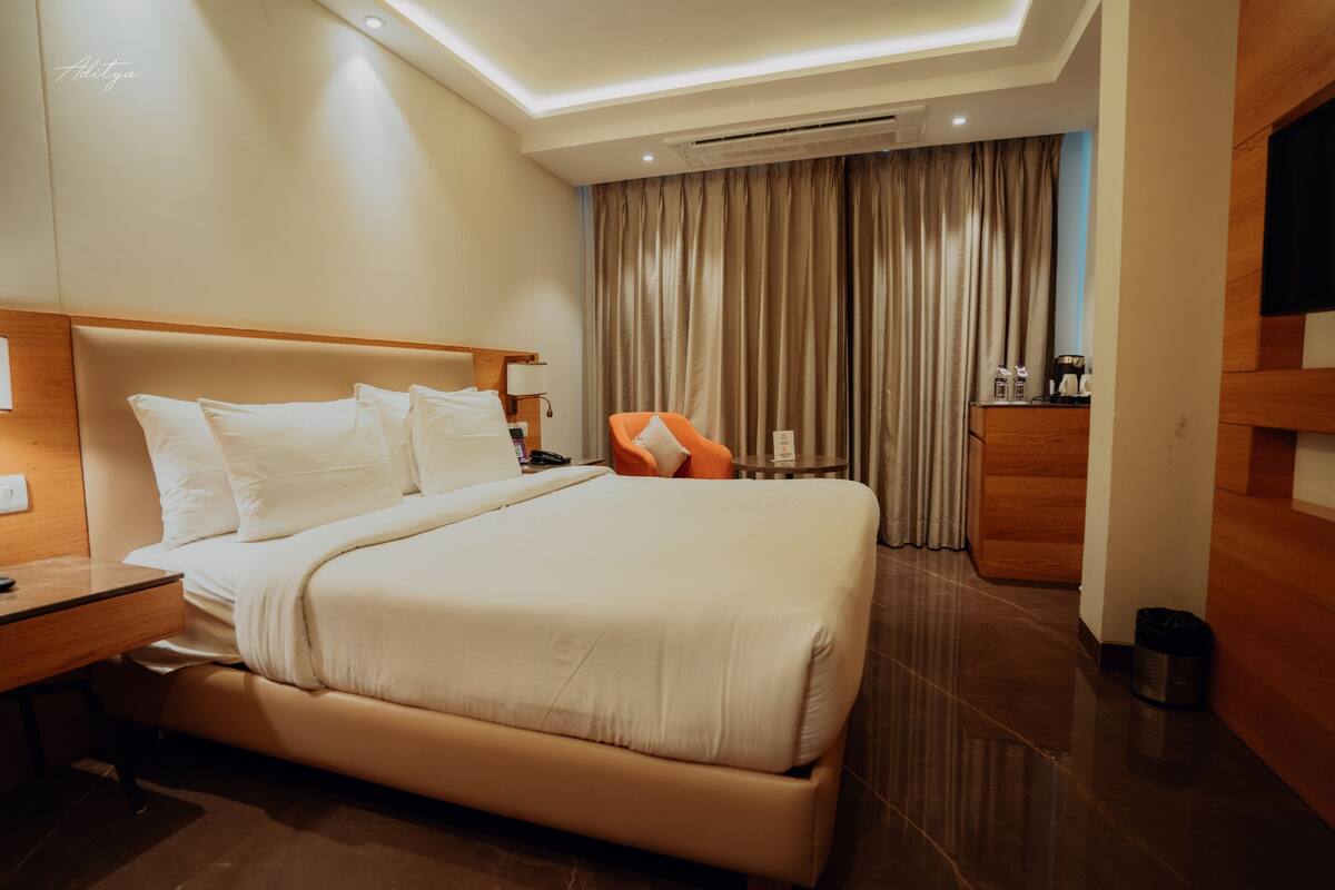 A modern hotel room with a large bed, a wooden desk, a chair, a TV, and a bathroom with a curtain.