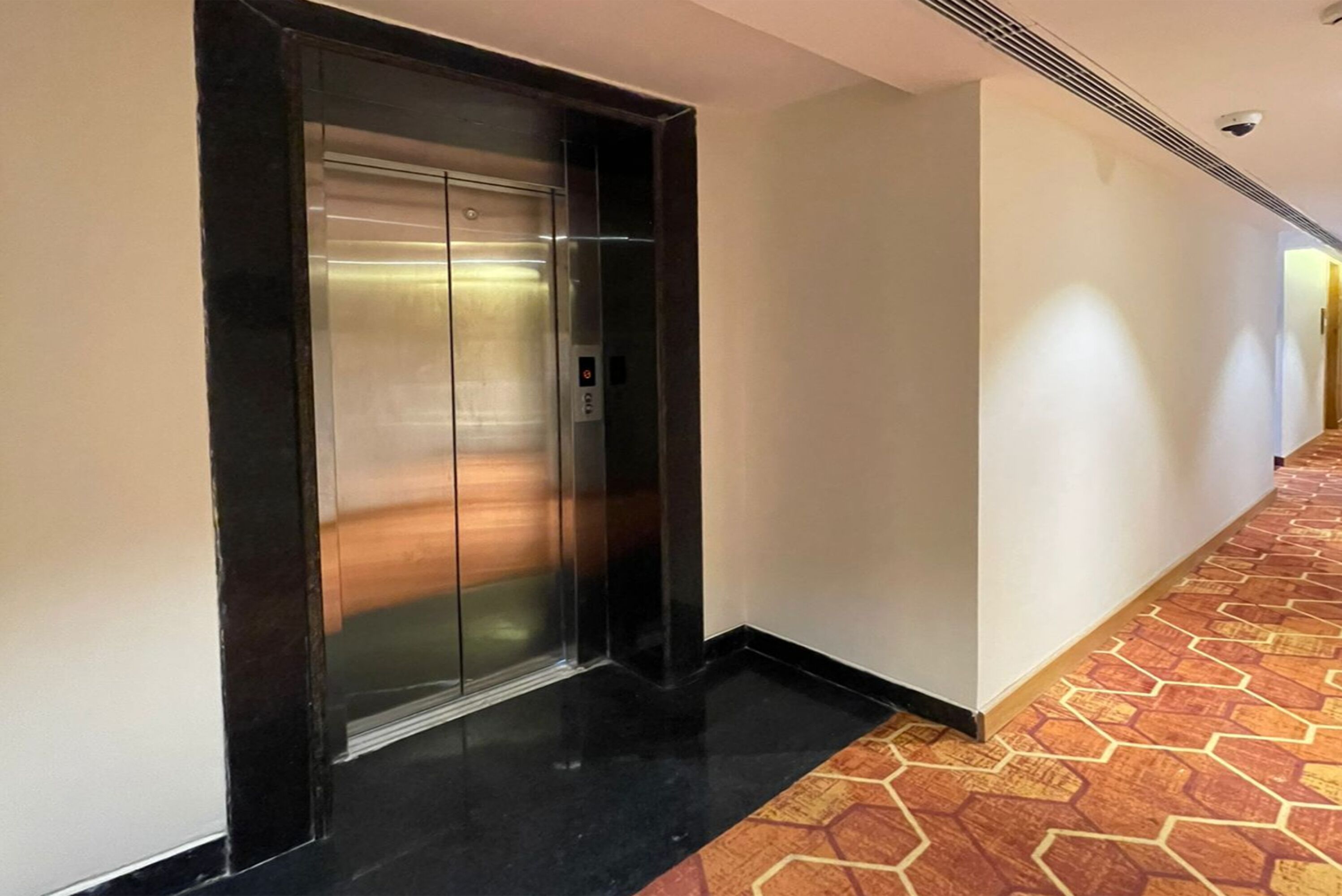 A hallway with a black elevator and patterned carpet.