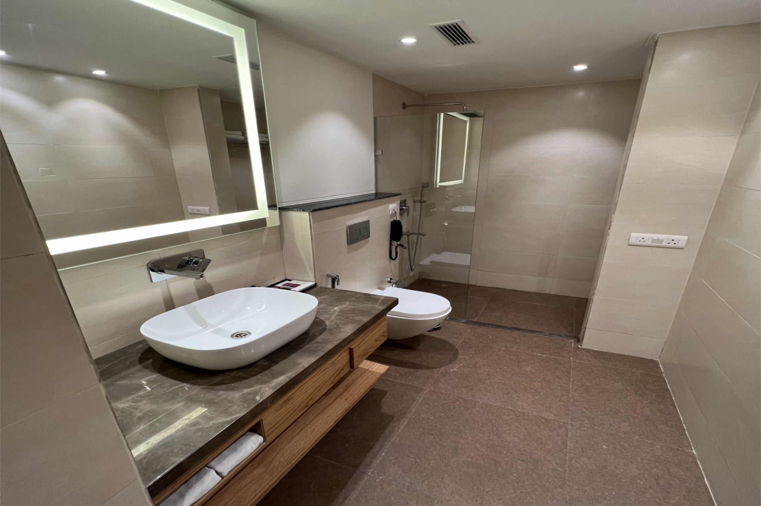 Un baño moderno con un espejo grande, un lavabo, un inodoro y una ducha con cerramiento de vidrio.